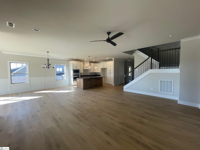 unfurnished living room featuring crown molding, dark wood-type flooring, and ceiling fan with notable chandelier