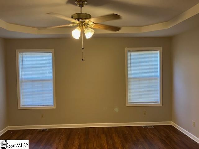 empty room with ceiling fan, a raised ceiling, and dark wood-type flooring