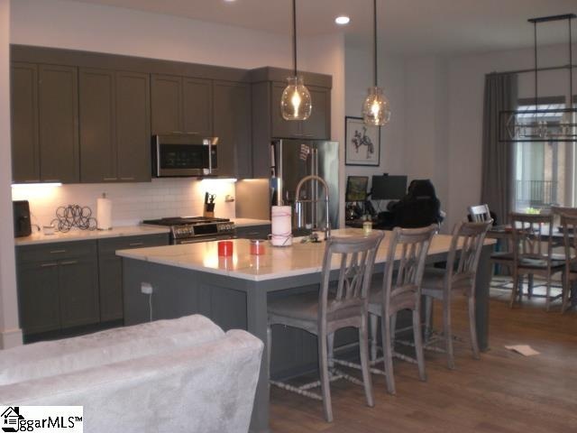 kitchen featuring hardwood / wood-style floors, a center island with sink, hanging light fixtures, appliances with stainless steel finishes, and a kitchen bar