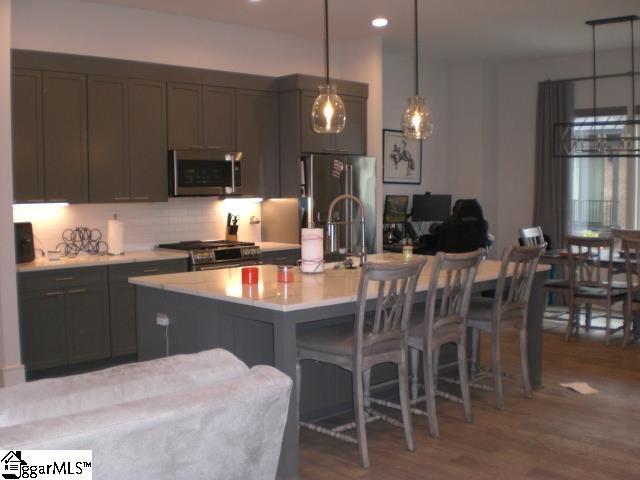 121 W Stone Ave Unit 15, Greenville, SC 29609 - kitchen featuring stainless steel appliances, light countertops, dark wood-style flooring, tasteful backsplash, and decorative light fixtures