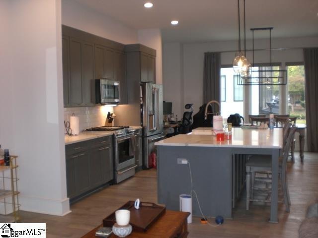 kitchen featuring sink, an island with sink, appliances with stainless steel finishes, decorative light fixtures, and light hardwood / wood-style floors