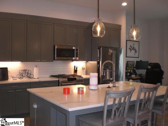 kitchen featuring pendant lighting, a breakfast bar, decorative backsplash, an island with sink, and appliances with stainless steel finishes