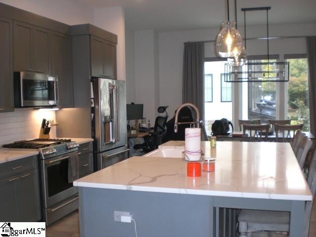 kitchen with pendant lighting, a kitchen island with sink, sink, appliances with stainless steel finishes, and light stone counters