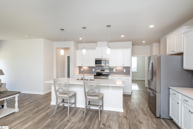 kitchen with stainless steel appliances, light hardwood / wood-style floors, decorative light fixtures, a center island with sink, and white cabinets