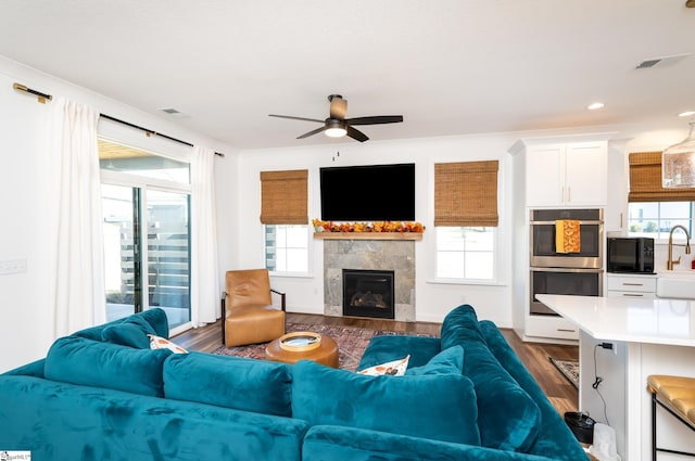 living room featuring a tile fireplace, a wealth of natural light, dark wood-type flooring, and ceiling fan