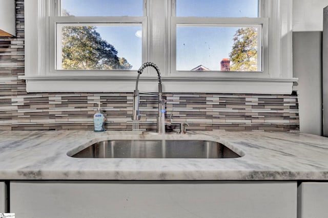 interior details with decorative backsplash, light stone countertops, and sink