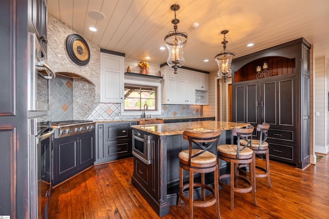 kitchen featuring pendant lighting, a breakfast bar, a center island, dark wood-type flooring, and light stone counters