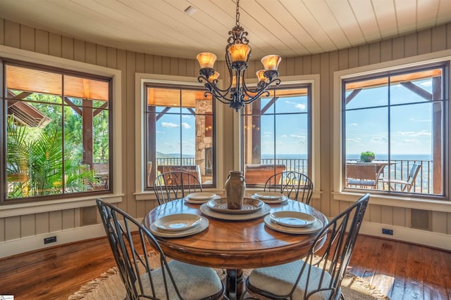 dining room featuring a notable chandelier, wood walls, a water view, and dark wood-type flooring