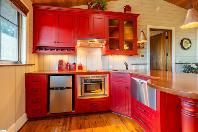 kitchen with decorative light fixtures, wood walls, lofted ceiling, and appliances with stainless steel finishes