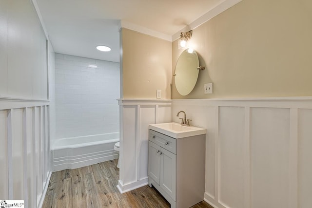 full bathroom featuring ornamental molding, tiled shower / bath combo, vanity, hardwood / wood-style floors, and toilet