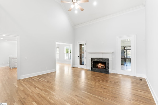 unfurnished living room featuring ceiling fan, crown molding, light hardwood / wood-style flooring, a fireplace, and a high ceiling