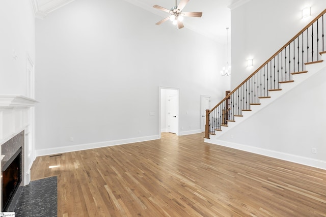 unfurnished living room with a high ceiling, hardwood / wood-style flooring, ceiling fan, ornamental molding, and a tiled fireplace