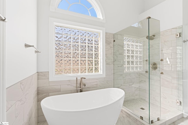 bathroom featuring a wealth of natural light, independent shower and bath, and tile walls