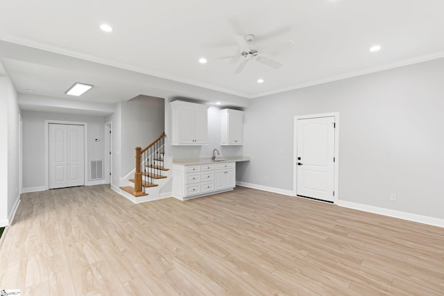 basement featuring ceiling fan, sink, light wood-type flooring, and crown molding