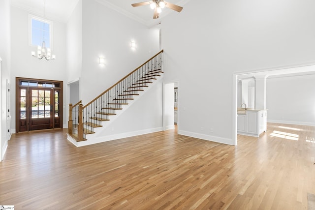 entryway featuring ceiling fan with notable chandelier, light hardwood / wood-style floors, ornamental molding, and a high ceiling