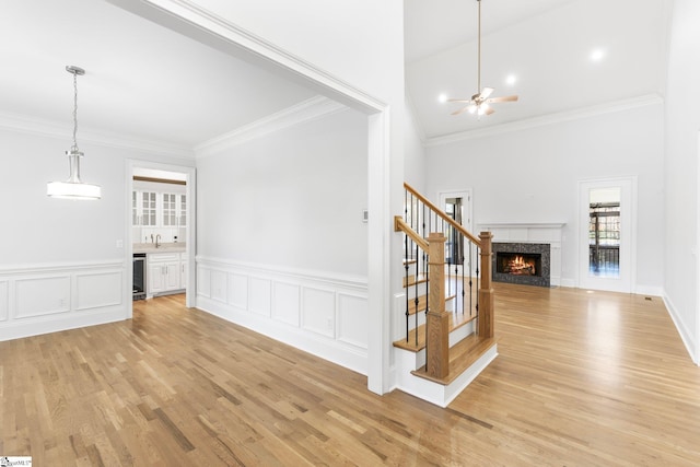 unfurnished living room with wine cooler, ceiling fan, light hardwood / wood-style flooring, and ornamental molding