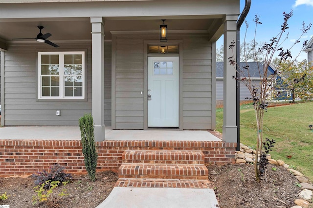 view of exterior entry featuring a porch, ceiling fan, and a lawn