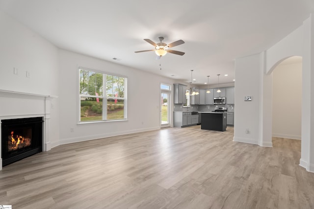 3361 Navin Trl, Roebuck, SC 29376 - unfurnished living room featuring a ceiling fan, arched walkways, light wood-type flooring, a warm lit fireplace, and baseboards