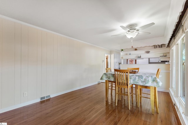 dining space featuring wooden walls, dark hardwood / wood-style floors, ceiling fan, and crown molding