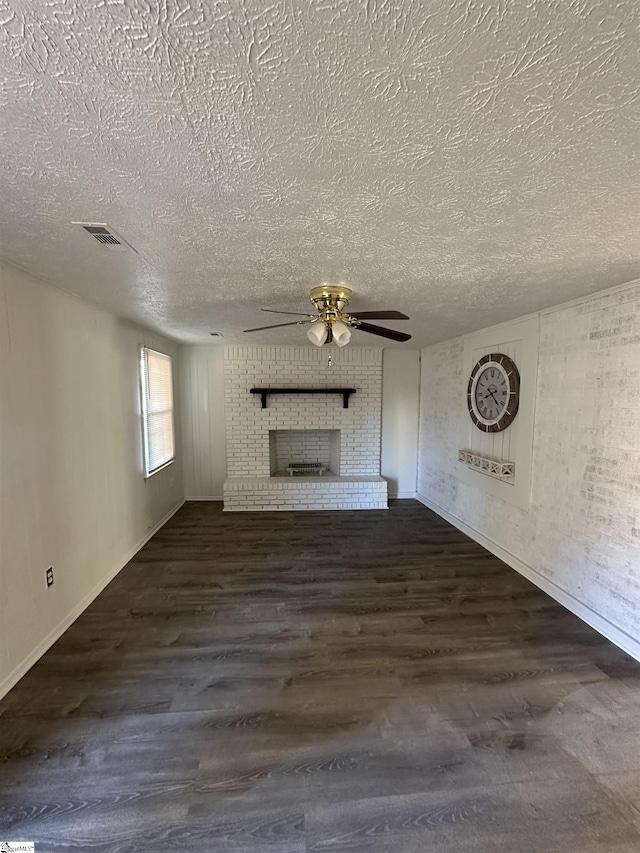 unfurnished living room with a textured ceiling, dark hardwood / wood-style floors, a brick fireplace, and ceiling fan