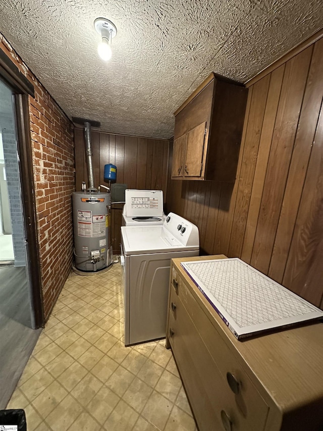 laundry room featuring cabinets, brick wall, gas water heater, washing machine and dryer, and wood walls