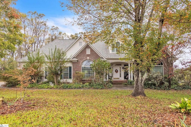 view of front of house featuring roof with shingles, brick siding, and a front lawn