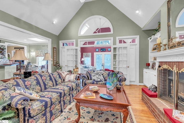 living area featuring high vaulted ceiling, light wood finished floors, and a brick fireplace