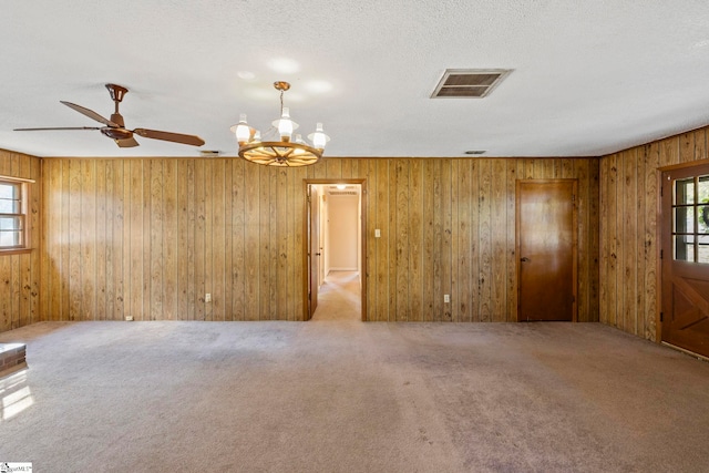 carpeted spare room with a textured ceiling, ceiling fan with notable chandelier, and wooden walls