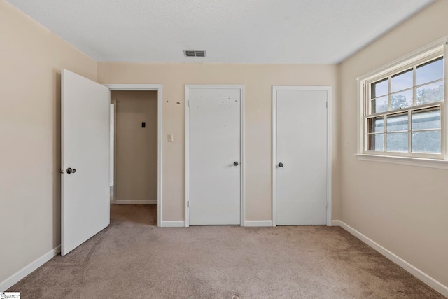 unfurnished bedroom featuring light carpet, a textured ceiling, and two closets