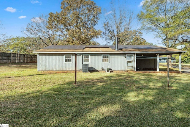 rear view of house featuring central AC unit, solar panels, and a yard