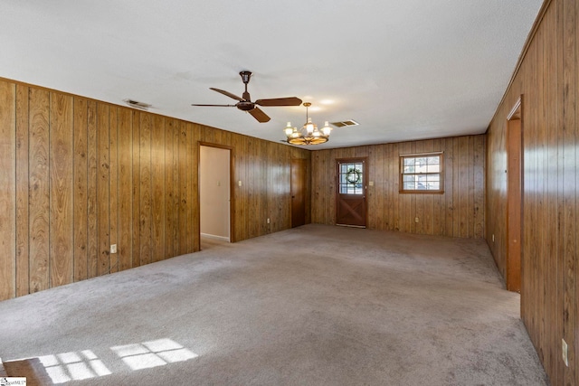 carpeted spare room with wooden walls and a notable chandelier