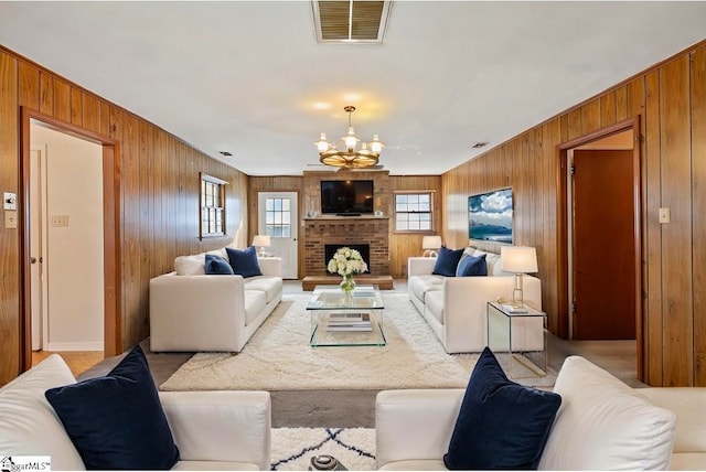 living room featuring a notable chandelier, a fireplace, wooden walls, and light carpet