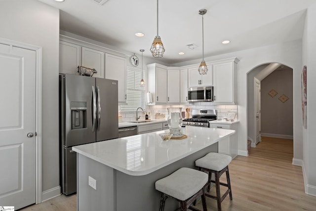 kitchen with pendant lighting, a center island, white cabinets, light wood-type flooring, and appliances with stainless steel finishes