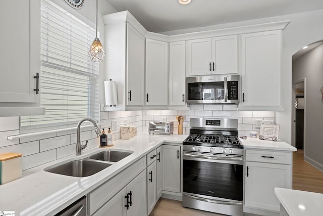 kitchen with white cabinetry, sink, hanging light fixtures, decorative backsplash, and appliances with stainless steel finishes