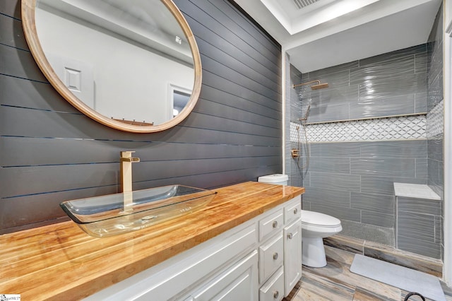 bathroom with tiled shower, vanity, toilet, and wooden walls