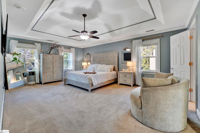 bedroom featuring light carpet, a tray ceiling, multiple windows, and ceiling fan