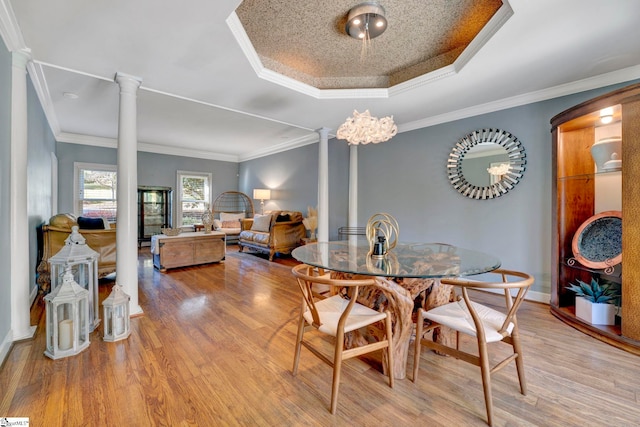 dining space with a raised ceiling, ornate columns, crown molding, and light wood-type flooring