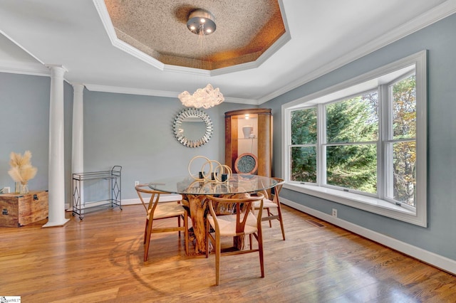 dining space featuring hardwood / wood-style floors, decorative columns, ornamental molding, and a tray ceiling