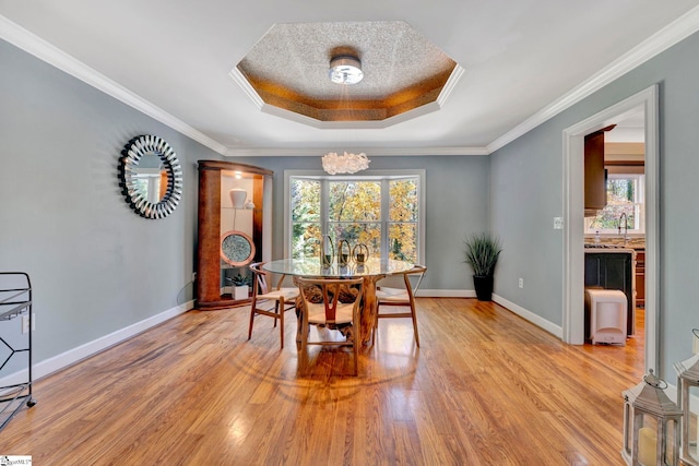 dining space featuring a tray ceiling, crown molding, sink, light hardwood / wood-style flooring, and a chandelier