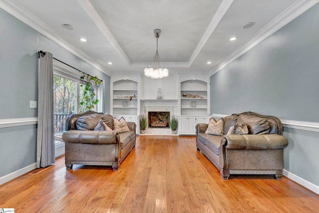 living room featuring an inviting chandelier, a raised ceiling, crown molding, a fireplace, and light hardwood / wood-style floors