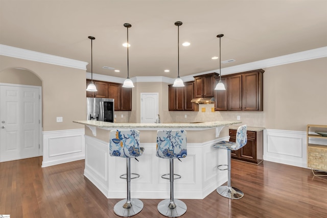 kitchen featuring light stone countertops, dark wood-type flooring, hanging light fixtures, a kitchen breakfast bar, and stainless steel fridge with ice dispenser