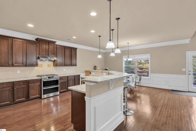 kitchen with a kitchen breakfast bar, dark hardwood / wood-style flooring, light stone counters, gas stove, and an island with sink