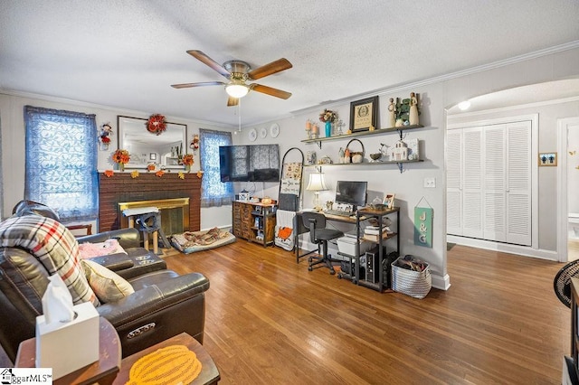 living room with a textured ceiling, ceiling fan, crown molding, hardwood / wood-style flooring, and a fireplace