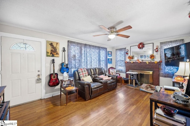 living room featuring hardwood / wood-style floors, ceiling fan, crown molding, and a brick fireplace