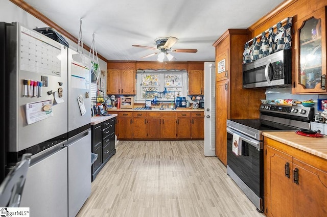 kitchen with appliances with stainless steel finishes, light hardwood / wood-style flooring, ceiling fan, and crown molding