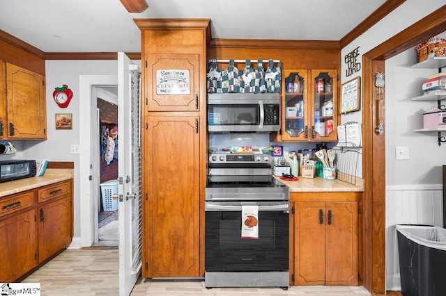 kitchen with crown molding, light hardwood / wood-style flooring, stainless steel appliances, and wood walls