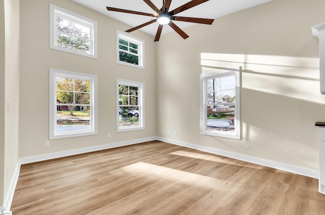 unfurnished living room featuring a towering ceiling, light hardwood / wood-style floors, and ceiling fan