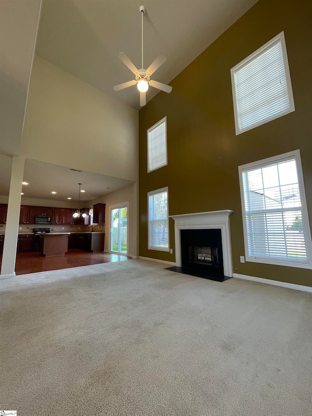 unfurnished living room featuring ceiling fan, a towering ceiling, and light carpet