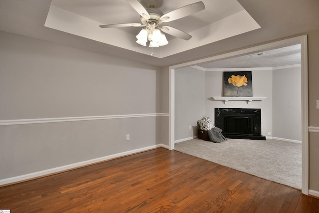 unfurnished living room with a raised ceiling, crown molding, ceiling fan, and wood-type flooring