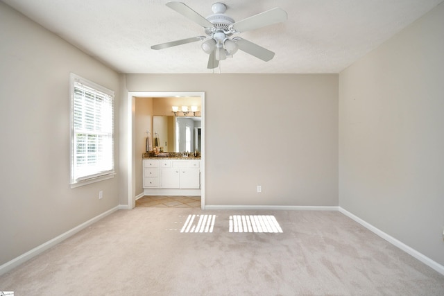 unfurnished bedroom featuring ceiling fan, sink, ensuite bathroom, light colored carpet, and a textured ceiling